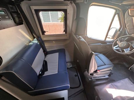 Spacious RV rental interior with bench seating, driver's cockpit, side window, & power management panel.