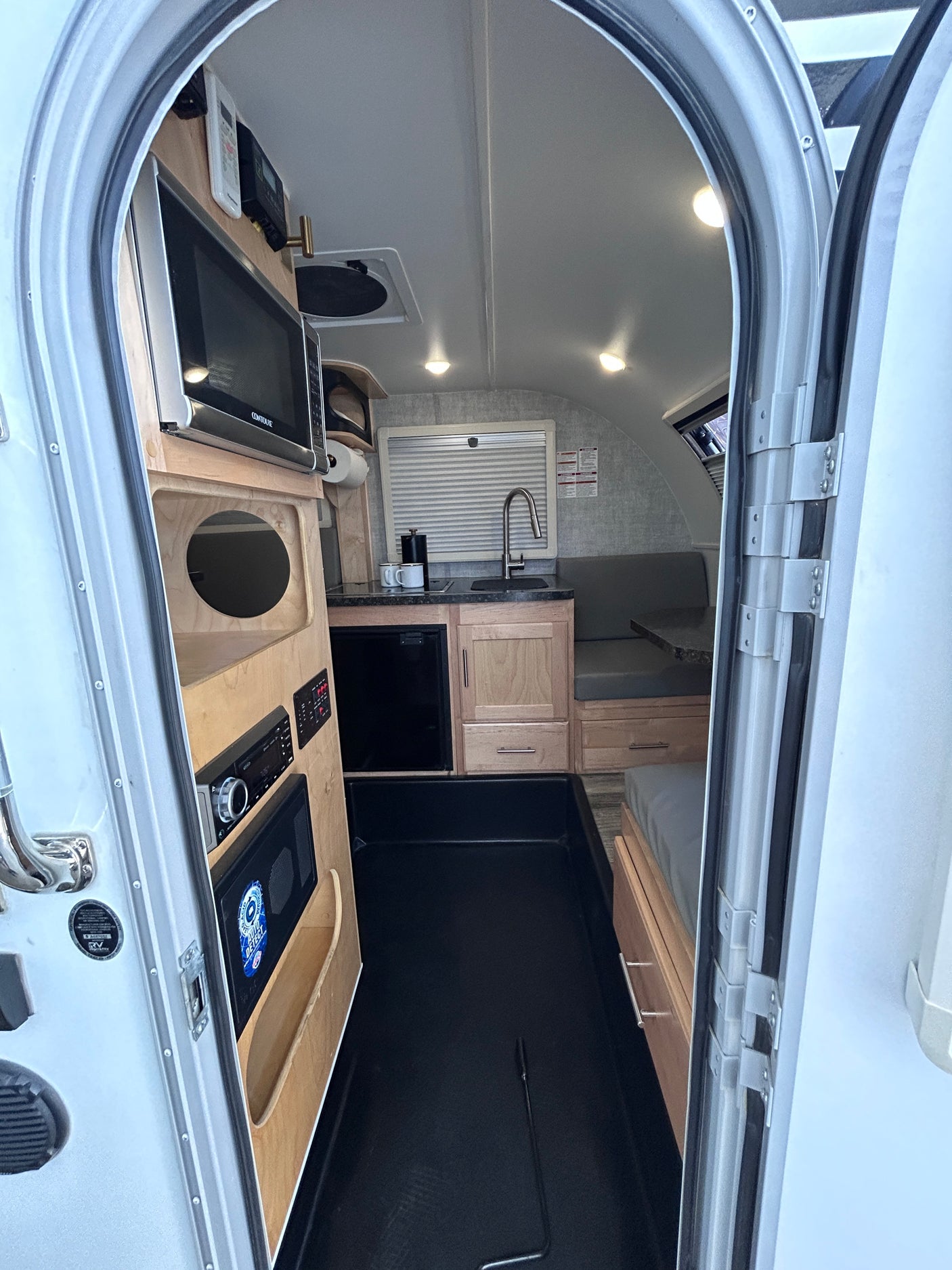 Brightly lit compact RV rental interior, seen from the door. Features a kitchen, dinette, microwave, and fridge.