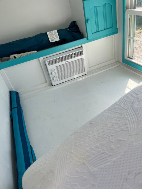 RV rental interior: a bright, compact space with white bedding, a Midea AC unit, and storage for essentials.