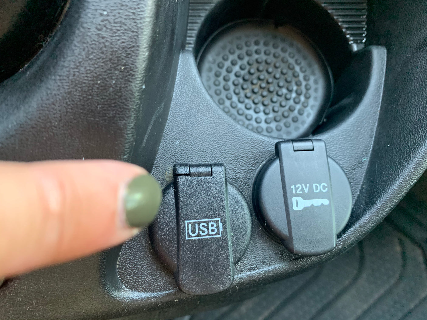 RV rental: Close-up of vehicle interior showing USB and 12V DC power ports and a cupholder. A finger points to the USB port.