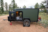 Compact green rv rental, a travel trailer, set up for camping. Doors open reveal a bed; rear galley shows stored items. Perfect for outdoor adventures.