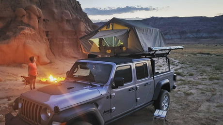 Camping in the desert: A Jeep Gladiator with rooftop tent, campfire, and child. Book your RV rental adventure!