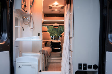 Interior of an rv rental camper van. From the rear, view of compact bath, living area, and driver's cab. Ready for travel!