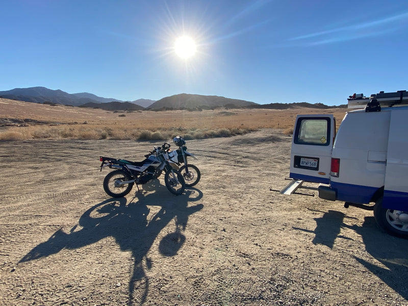 Two dirt bikes await adventure beside an RV rental van with a ramp in a sunny, arid mountain landscape. Ideal for desert exploration. — photo 20