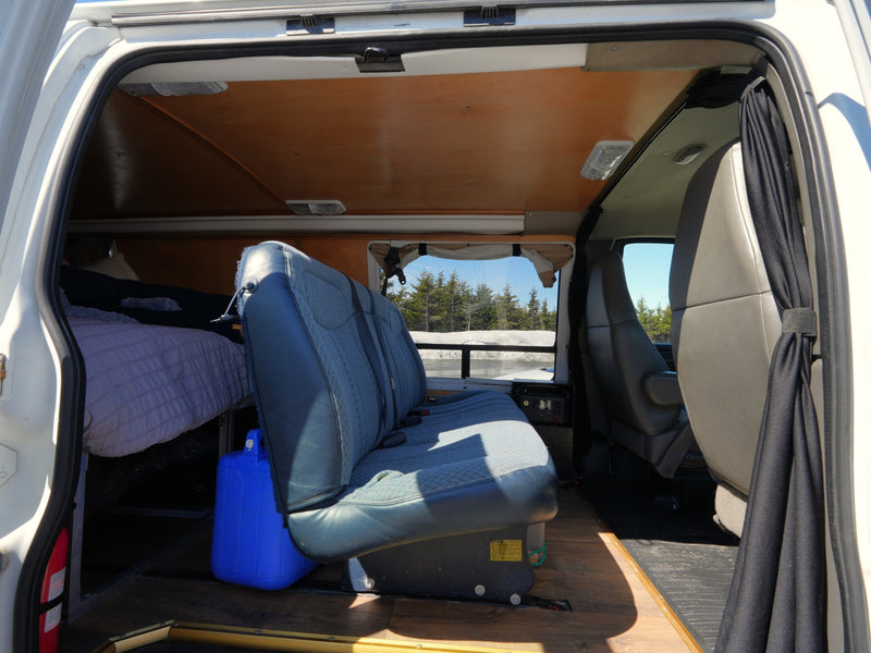 Inside a spacious RV rental camper van, featuring a comfortable bed, rear bench seat, and scenic winter window view. — photo 8