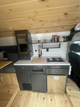 Inside a stylish RV rental, featuring a compact kitchen with stove, sink, fridge, and wooden accents.