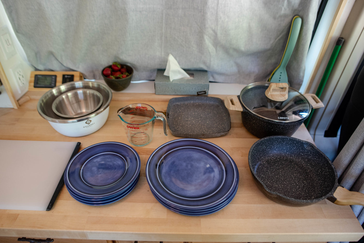 Inside an RV rental: a compact kitchen counter with blue plates, mixing bowls, Pyrex measuring cup, and speckled pots & pans.