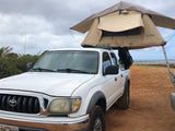 White Toyota truck with an overland rooftop tent set up on a sandy beach. Ideal for your next rv rental adventure!