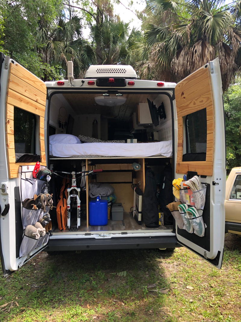 This custom RV rental van's open rear reveals a raised bed, bike storage, and door organizers. Perfect for adventure trips. — photo 5