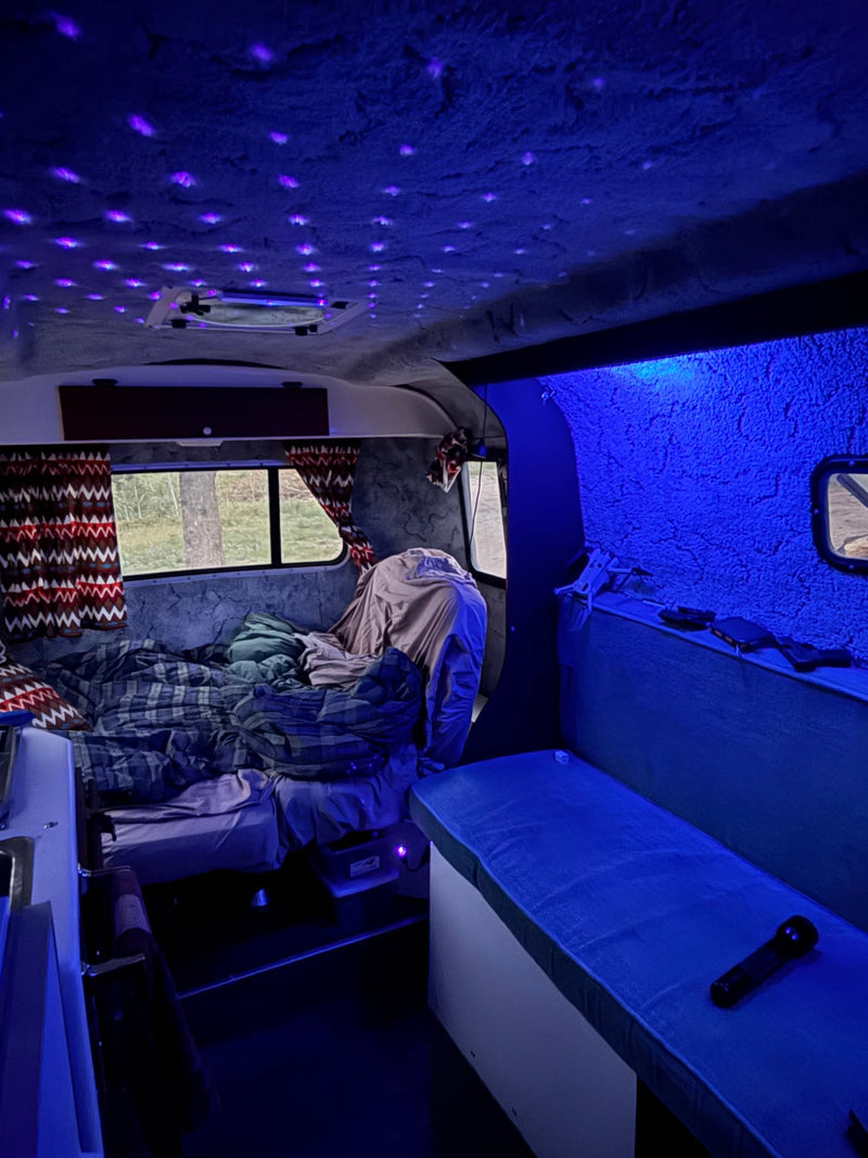  and windows looking out to a mountain forest view.|Relaxing inside a cozy RV rental. Legs are visible on a bed with a plaid blanket — photo 9