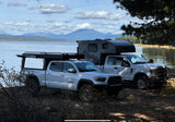 Lakeside truck camping: a silver Tacoma and white Ford, both with off-road campers, ready for your RV rental journey.