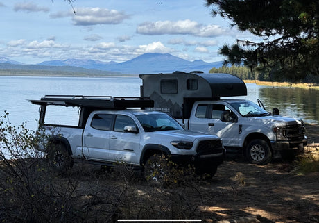 Lakeside truck camping: a silver Tacoma and white Ford, both with off-road campers, ready for your RV rental journey.