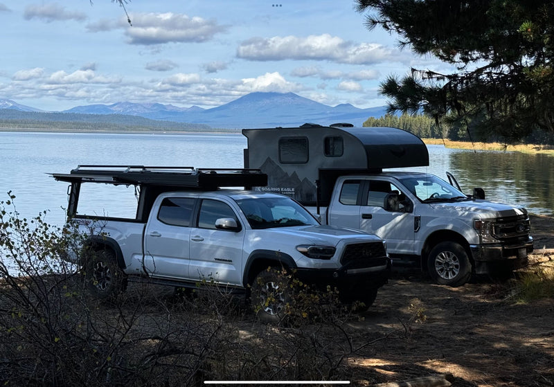  in a forest setting.|Frosted RV rental truck camper parked at a misty lakeside campsite. Ideal for outdoor adventures.|Enjoy nature with this truck camper and Tacoma with rooftop tent parked lakeside. An ideal RV rental for overlanding adventures.|White truck with Soaring Eagle truck camper (an RV rental type) — photo 7