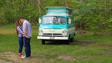 Embracing couple with a vintage turquoise & white Dodge camper van. Ideal RV rental for romantic adventures!