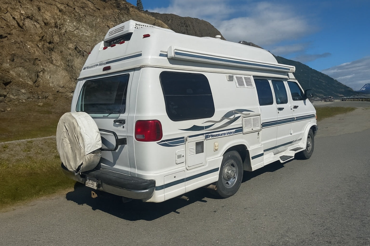 White Pleasure-Way camper van, a popular RV rental, parked on a paved road with mountains in the distance, perfect for scenic travel. — photo 9
