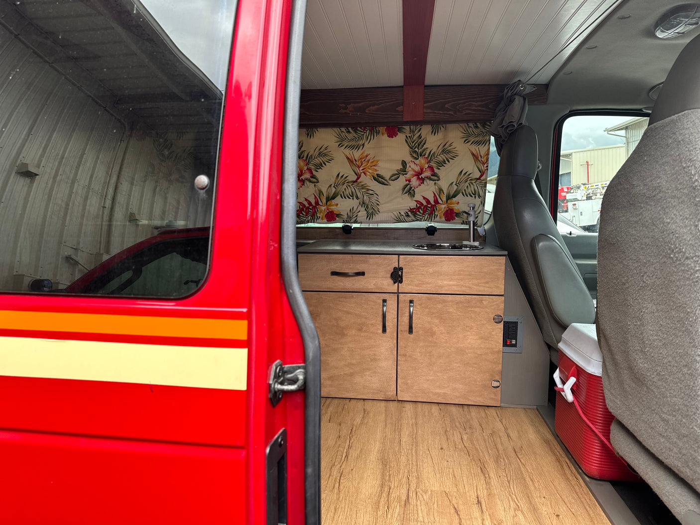 Open side door view of our RV rental. Inside: a custom van kitchen, wood floor, tropical curtain, & front seats.