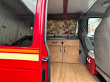 Open side door view of our RV rental. Inside: a custom van kitchen, wood floor, tropical curtain, & front seats.