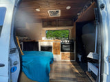 Inside a unique RV rental: wood-paneled van conversion with full kitchen, bed, and custom storage for adventure.