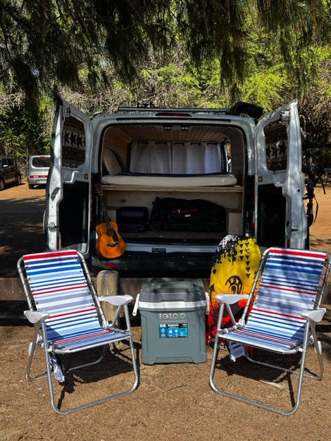 This RV rental camper van set up for adventure: open back reveals a cozy bed, guitar, cooler, and chairs for outdoor enjoyment.