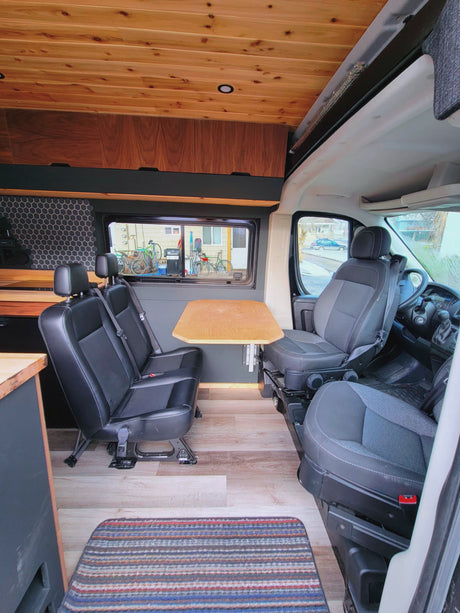 RV rental: Inside a camper van featuring a dining area with two rear-facing seats, a table, and wooden decor.