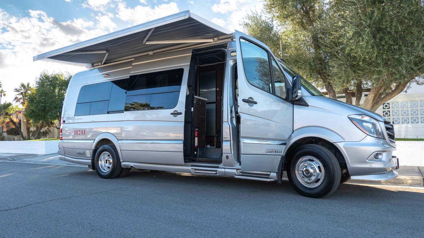 A modern silver camper van, an ideal rv rental, is parked with its awning extended and side door open on an asphalt road.