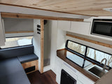 RV rental interior featuring a modern kitchen with sink, stove, & microwave, cozy U-shaped seating, and warm wood accents.