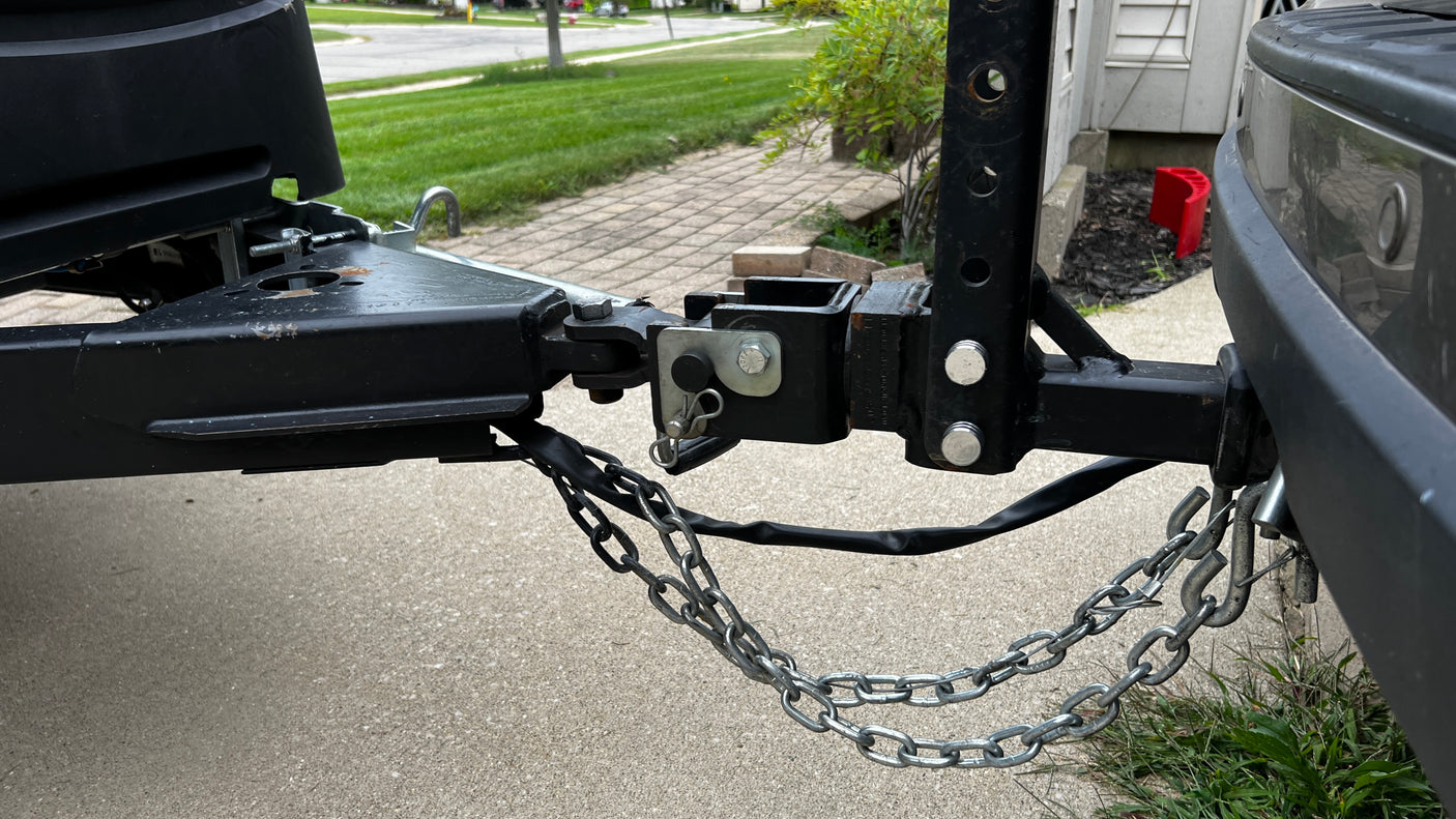A close-up view of an RV rental's trailer hitch, coupler, and safety chains securely connected to a towing vehicle.