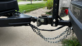 A close-up view of an RV rental's trailer hitch, coupler, and safety chains securely connected to a towing vehicle.