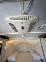 RV rental pop-up camper interior: Ceiling AC unit visible above a cozy sleeping area with bed and pillows.