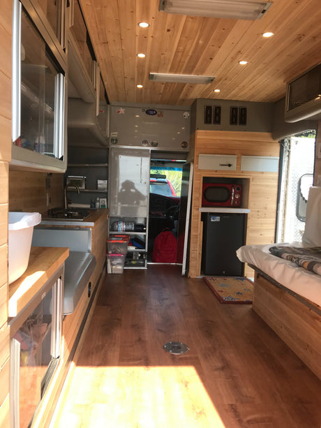 Cozy RV rental interior with wood finishes, compact kitchen, and comfortable bed, perfect for mobile adventures.