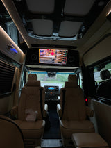 Luxury rv rental interior: plush captains' chairs, large screen with Bloomberg TV, ambient lighting. Ready for a comfortable ride.