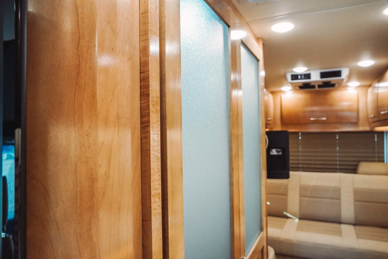Bright RV rental interior: light wood panels, frosted glass partition, and a beige seating area with overhead cabinets. — photo 9
