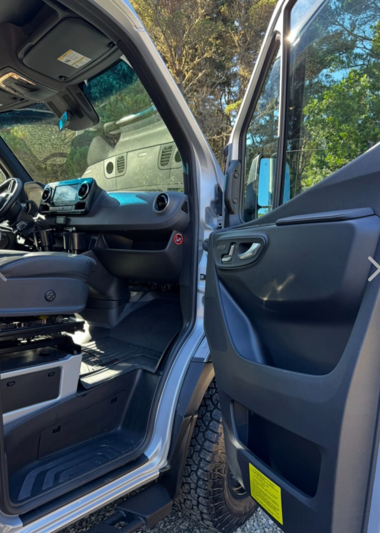  a dog on a leash nearby.|Silver Mercedes-Benz Sprinter camper van parked among tall trees. Ready for your next RV rental adventure!|Experience freedom with this RV rental camper van! Rear view showing open doors — photo 3