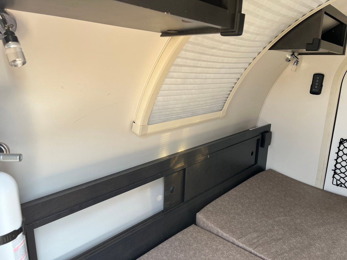 Cozy interior of an RV rental: a bed with grey cushions, curved window with blinds, and reading lights. — photo 14