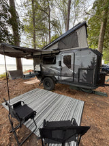 Lakeside RV rental: Modern teardrop camper setup with outdoor kitchen, pop-up tent, awning, chairs, and rug for camping.