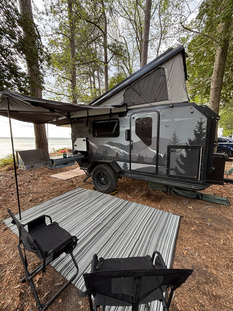 Lakeside RV rental: Modern teardrop camper setup with outdoor kitchen, pop-up tent, awning, chairs, and rug for camping.