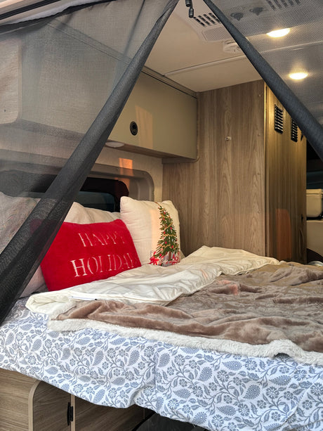 Inside a cozy RV rental: bed with festive holiday pillows, patterned sheets, and mosquito net for comfort.
