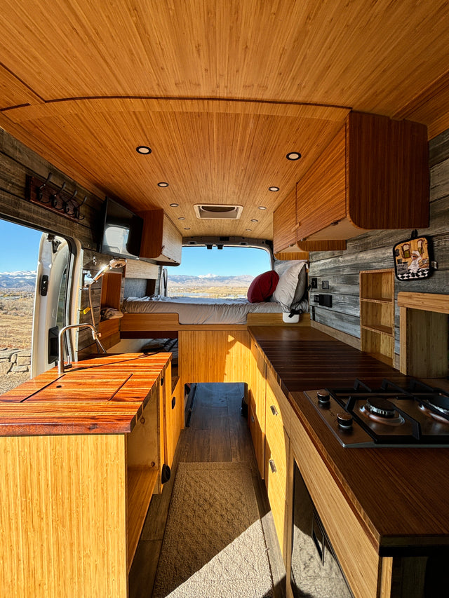 Cozy camper van interior with bamboo finishes, kitchenette, bed, and a scenic mountain view, perfect for your next rv rental adventure.