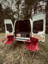 White camper van, customized with bed and storage, opens to two red camping chairs. Perfect for your next RV rental adventure.