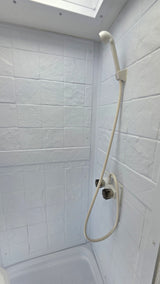 Clean, white shower stall in an RV rental, featuring a handheld showerhead, faucets, and textured tile-like walls.