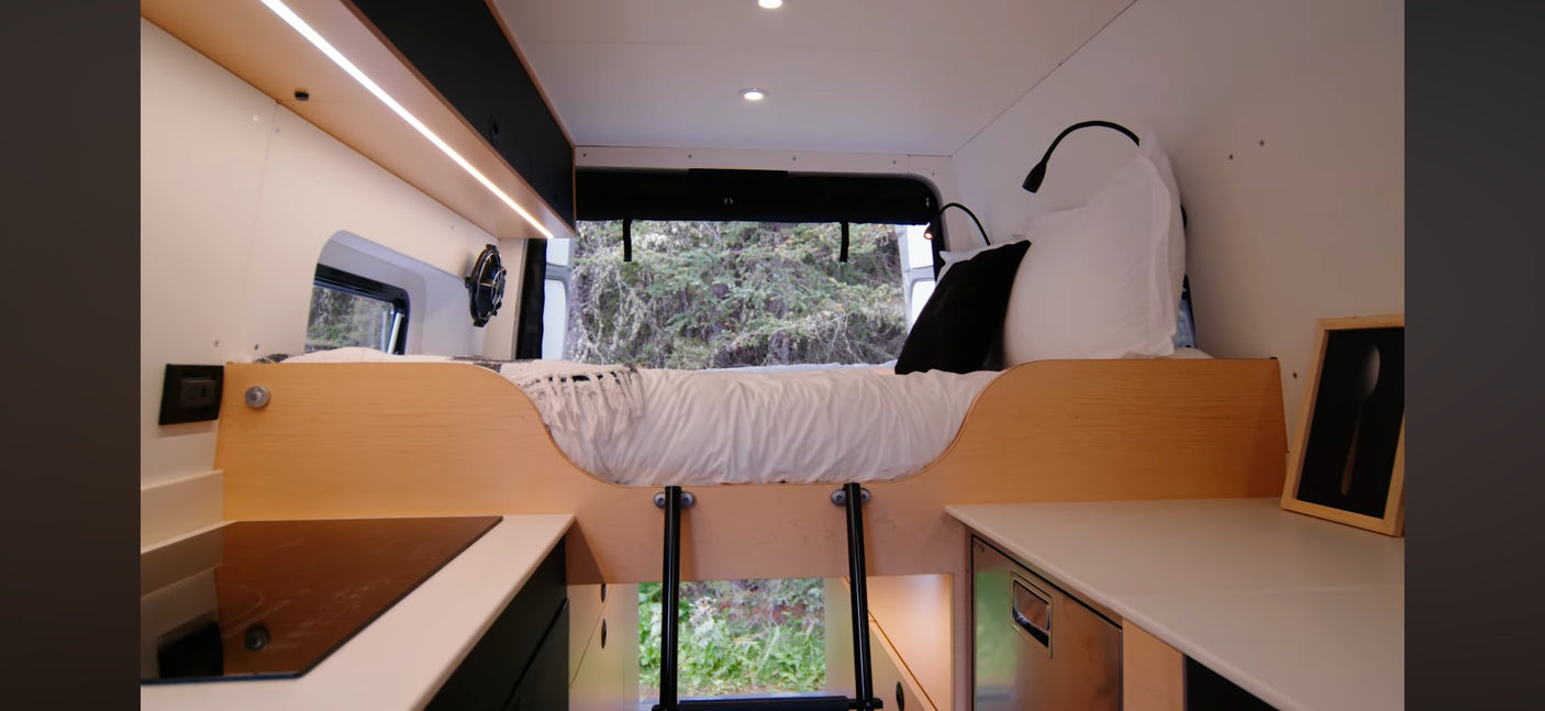 RV rental interior: A compact camper van with a raised bed, ladder, modern kitchenette, and window views of nature.