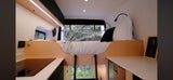 RV rental interior: A compact camper van with a raised bed, ladder, modern kitchenette, and window views of nature.