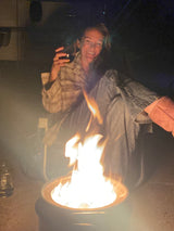 Smiling woman by a vibrant fire pit at night during an RV rental trip. For visually impaired: A bright fire illuminates the outdoor scene.