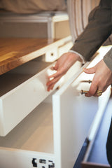 Hands open white storage drawers in an RV rental. These compact built-in compartments offer convenient interior organization.