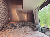 Cozy RV rental bedroom with patterned bedding, metallic walls, and a view of the forest outside the window.