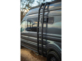 Dark gray custom RV rental van with a side-mounted ladder and roof rack, parked outdoors.