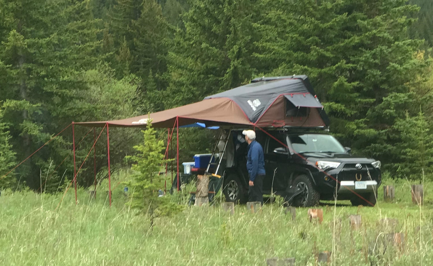 An SUV with a rooftop tent and awning, set up for overlanding, provides a unique RV rental experience. A man stands beside it. — photo 14