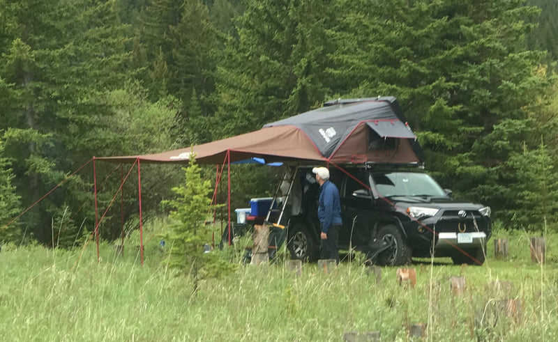 An SUV with a rooftop tent and awning, set up for overlanding, provides a unique RV rental experience. A man stands beside it. — photo 14