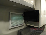 RV rental bedroom: wall-mounted TV, window with blinds, and overhead storage cabinets for compact living.