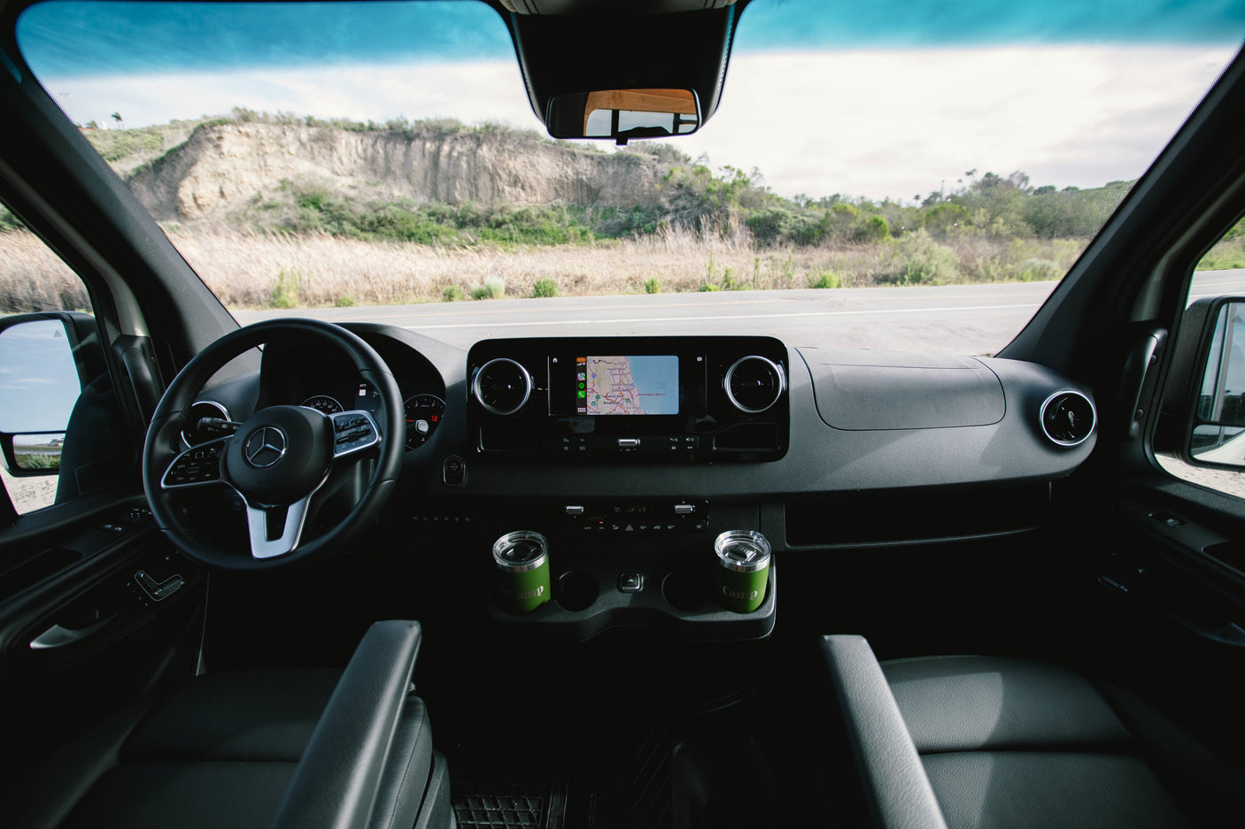 RV rental interior: Dashboard, nav screen (CA map), and green mugs. Road ahead visible for your next adventure.